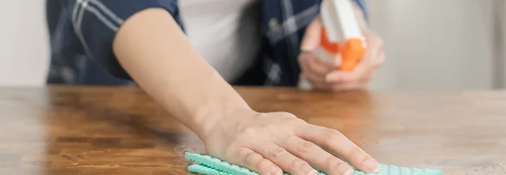 Person reinigt Holztisch mit Tuch.